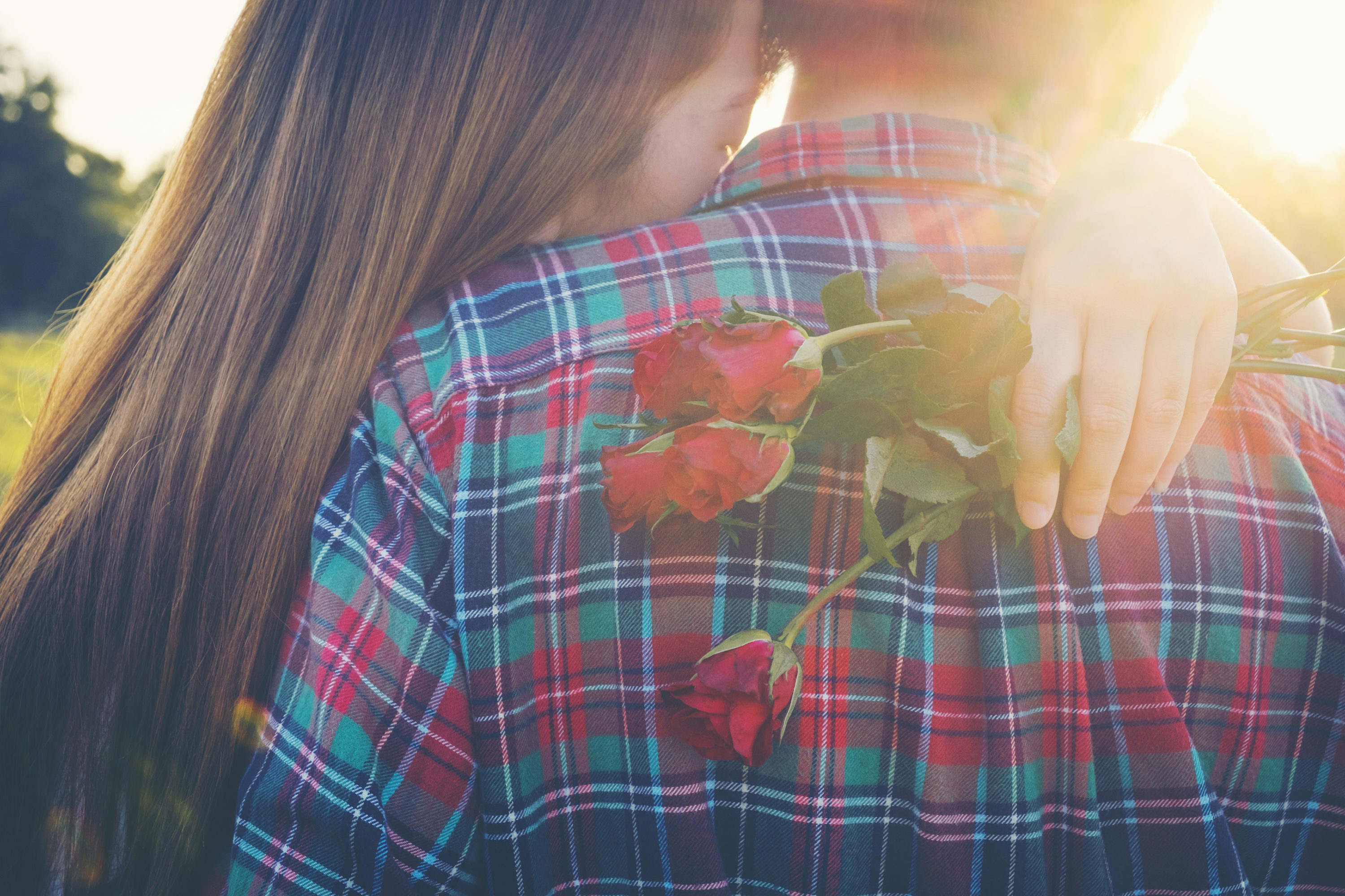 A young women holding roses embraces a man